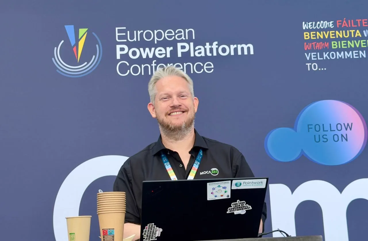 Pointwork på European Power Platform Conference 2026 i Bella Center: en fra teamet ved MOCA365-standen foran konferencens væg, med en laptop med MOCA365- og Pointwork-mærkater.